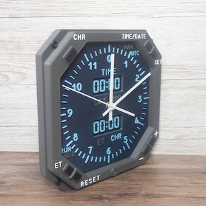 Pilot gift wall clock modeled after an Boeing aircraft cockpit chronometer. This aviation decor features realistic flight instrument details, a grey bezel, and digital time displays.