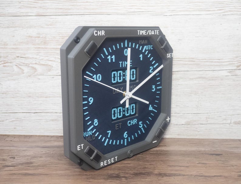 Pilot gift wall clock modeled after an Boeing aircraft cockpit chronometer. This aviation decor features realistic flight instrument details, a grey bezel, and digital time displays.