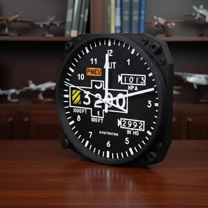 May include: Black aviation-themed clock with white numerals and hands. The clock face displays the numbers 1 through 12, along with the text "PNEU", "LIT", "HPA", and "IN HG". The clock reads 3200 and is set against a dark wooden surface.