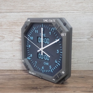 Pilot gift wall clock modeled after an Boeing aircraft cockpit chronometer. This aviation decor features realistic flight instrument details, a grey bezel, and digital time displays.