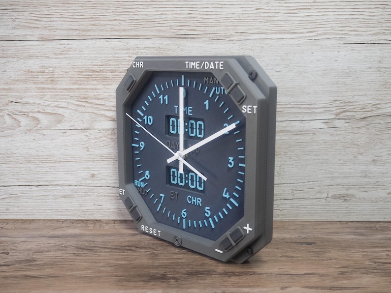 Pilot gift wall clock modeled after an Boeing aircraft cockpit chronometer. This aviation decor features realistic flight instrument details, a grey bezel, and digital time displays.