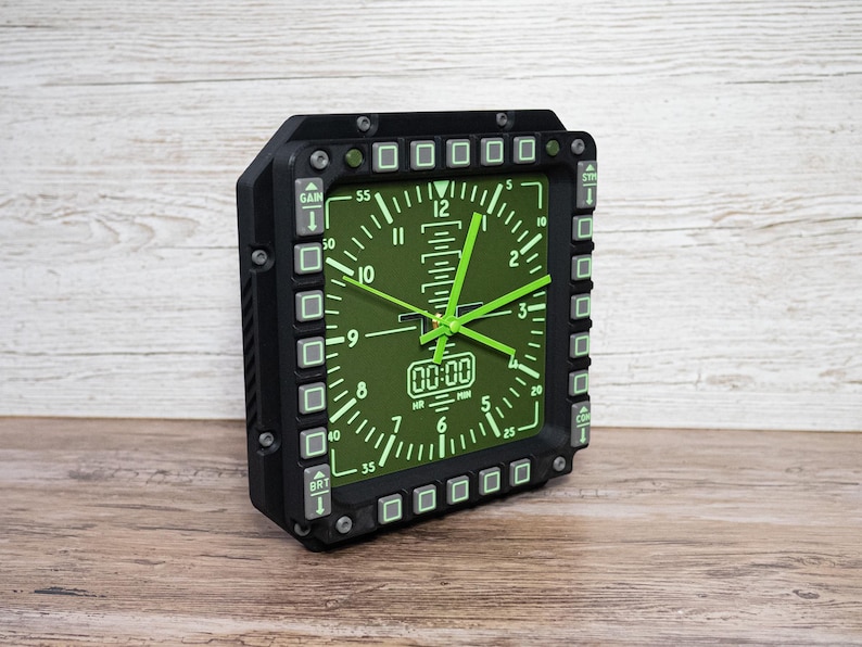 Fighter jet pilot wall clock in the style of a MFD (multi function display). Square black housing with light grey buttons and green lcd displaying time.