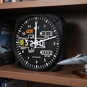 May include: Black aviation-themed clock with white markings and hands, displaying altitude and pressure readings. The clock is on a wooden shelf with model airplane and books.