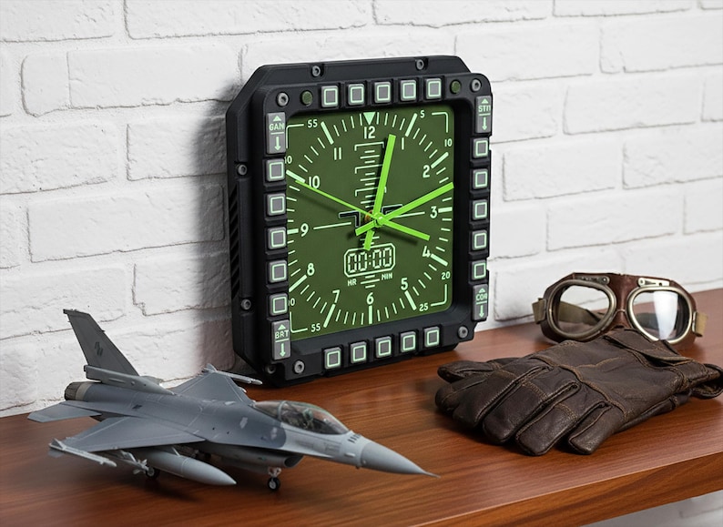 May include: Aviation-themed display with a black and green clock, model jet, brown leather gloves, and vintage aviator goggles. The clock has a square face with green hands and a black frame. The items are on a wooden surface.