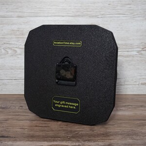 May include: A black, octagonal clock with a textured surface. The clock mechanism is visible on the back. Text on the back reads "AviationTime.etsy.com" and "Your gift message engraved here."