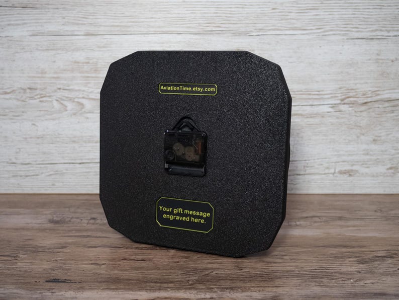 May include: A black, octagonal clock with a textured surface. The clock mechanism is visible on the back. Text on the back reads "AviationTime.etsy.com" and "Your gift message engraved here."
