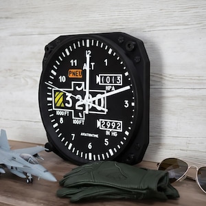 May include: A black aviation-style wall clock with white numerals and hands, showing altitude and pressure readings. A model aircraft, green gloves, and sunglasses are also visible. The clock reads 975 metres.