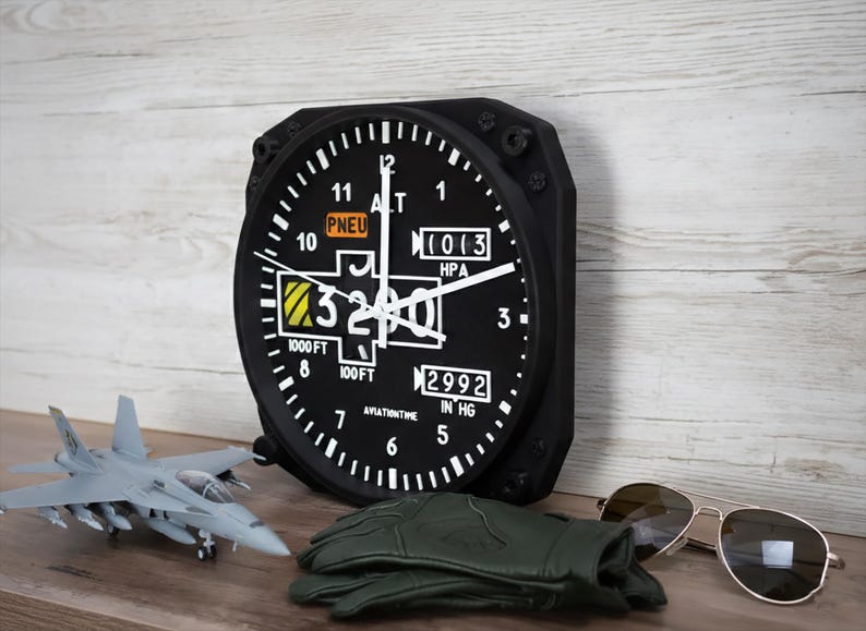 May include: A black aviation-style wall clock with white numerals and hands, showing altitude and pressure readings. A model aircraft, green gloves, and sunglasses are also visible. The clock reads 975 metres.