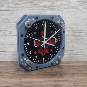 Pilot gift wall clock modeled after an Airbus aircraft cockpit chronometer. This aviation decor features realistic flight instrument details, a grey bezel, and digital time displays.