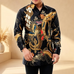 Könnte beinhalten: Ein langärmeliges, schwarzes Hemd mit Knopfleiste und einem detaillierten Batik-Muster in Gold, Weiß und Rot. Das Design zeigt komplexe Vogelmotive, geschwungene organische Formen und florale Elemente auf der Vorderseite und den Ärmeln.
