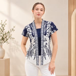 May include: A short-sleeved open-front jacket featuring a navy blue and white batik-style pattern with stylised bird and floral motifs. The garment has a solid navy blue inner layer and a vertical border design along the front opening edges.