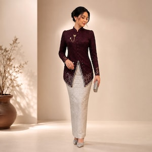 May include: A dark burgundy long-sleeved lace top with a front button closure and a gold butterfly brooch, paired with a floor-length, light grey, textured straight skirt. The outfit is completed with silver pointed-toe heels and a small silver clutch.