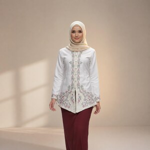 Peut inclure: Une femme porte un haut blanc à manches longues avec des broderies florales et une jupe bordeaux. Le haut présente des motifs floraux complexes en rose, vert et beige. Un hijab beige couvre la tête. La tenue est un mélange de styles traditionnels et modernes.