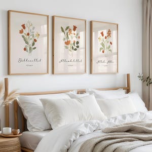 Puede incluir: Tres láminas botánicas enmarcadas con arreglos florales en tonos rojos, naranjas y verdes. Cada lámina tiene un marco de madera y presenta caligrafía árabe. Las láminas se exhiben sobre una cama con ropa de cama blanca.