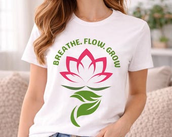 Puede incluir: Camiseta blanca con un diseño de flor de loto rosa y las palabras "Breathe. Flow. Grow." en verde. La camiseta se combina con vaqueros azules. El diseño presenta un loto y hojas estilizados.