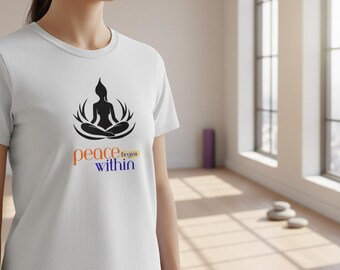 Puede incluir: Camiseta blanca con una silueta negra de una persona en posición de yoga sentada, con las palabras "peace begins within" en naranja y azul. La camiseta es de un material suave.
