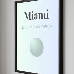May include: Framed art print featuring the city name "Miami" in a bold font, with coordinates 25.7617&deg;N, 80.1918&deg;W. The artwork has a gradient background and a circular design element. The frame is black.