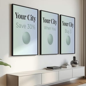 May include: Three framed posters with the text "Your City" in a bold font. Each poster has a different tagline: "Save 30%", "When You", and "Buy 3". Below, a white cabinet with books and a decorative vase.