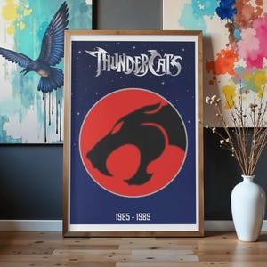 Puede incluir: Póster enmarcado con el logotipo de Thundercats. El diseño incluye el logotipo de Thundercats en plata, una silueta de gato negro sobre un círculo rojo y los años 1985-1989. El fondo es azul oscuro con estrellas blancas.