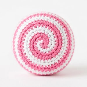 May include: A crocheted ball with a spiral design. The ball is a combination of pink and white yarn, creating a visually appealing pattern. The handmade item is likely a toy or decorative object.