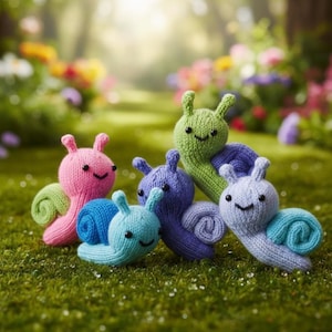May include: A group of five knitted snails in various colors: pink, green, blue, and purple. Each snail has a smiling face and a spiral shell. They are arranged on a bed of green grass, with a blurred background of flowers and trees.