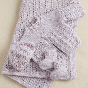 May include: A light purple knitted baby set comprising a blanket, cardigan, hat, and two booties. The set features a textured pattern and is made of soft yarn. The cardigan has three buttons.