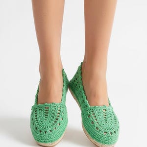 May include: Green crochet flats with a woven pattern. The shoes have a rounded toe and a natural-coloured sole. The flats are a bright, spring green colour.