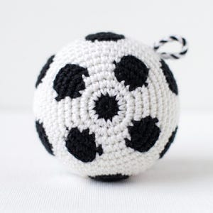 May include: A handmade crochet soccer ball in white with black pentagon shapes. The ball has a small loop for hanging. The stitches are tight and even, giving the ball a smooth texture. A classic sports-themed item.