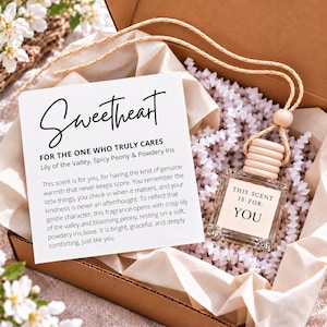 Peut inclure: Un flacon de parfum carré en verre avec un bouchon en bois clair et un cordon de suspension, placé dans une boîte avec du papier froissé blanc. Une carte blanche inclut le texte Sweetheart, For the one who truly cares et les notes olfactives.