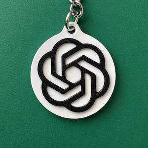 May include: A white and black keychain with a circular pendant. The pendant features a black, stylized flower design. The keychain has a silver-colored ring and chain.