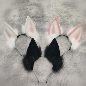 May include: Four headbands with animal ear designs. Two headbands have white ears with pink inner ear details, and two have black ears. The ears are made of fluffy faux fur and attached to thin black headbands.