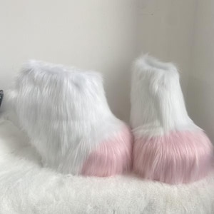 May include: A pair of fluffy, faux fur boots. The boots are primarily white with a soft pink color at the toe area. The boots are designed to be worn as part of a costume or for novelty purposes.