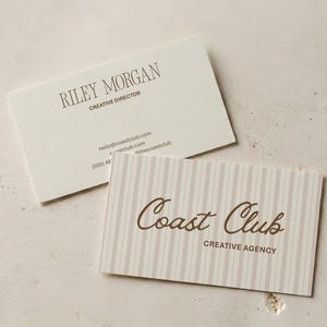 May include: Two rectangular business cards. One card is off-white with dark brown text reading Riley Morgan, Creative Director, and contact details. The second card features a light brown vertical stripe pattern with Coast Club Creative Agency.
