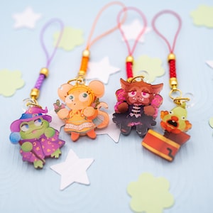 May include: Four acrylic charms with colorful character illustrations, each attached to a braided cord with a gold-tone metal bead. The charms feature a frog in a purple robe, a mouse in an orange dress, a furry creature with wings, and a clown in a box.
