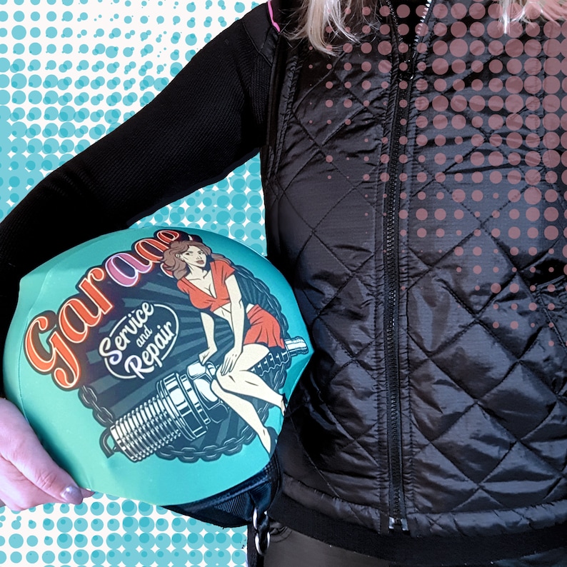 May include: A teal blue helmet cover with a vintage pinup girl design. The cover features the text "Garage Service and Repair" in a retro font.