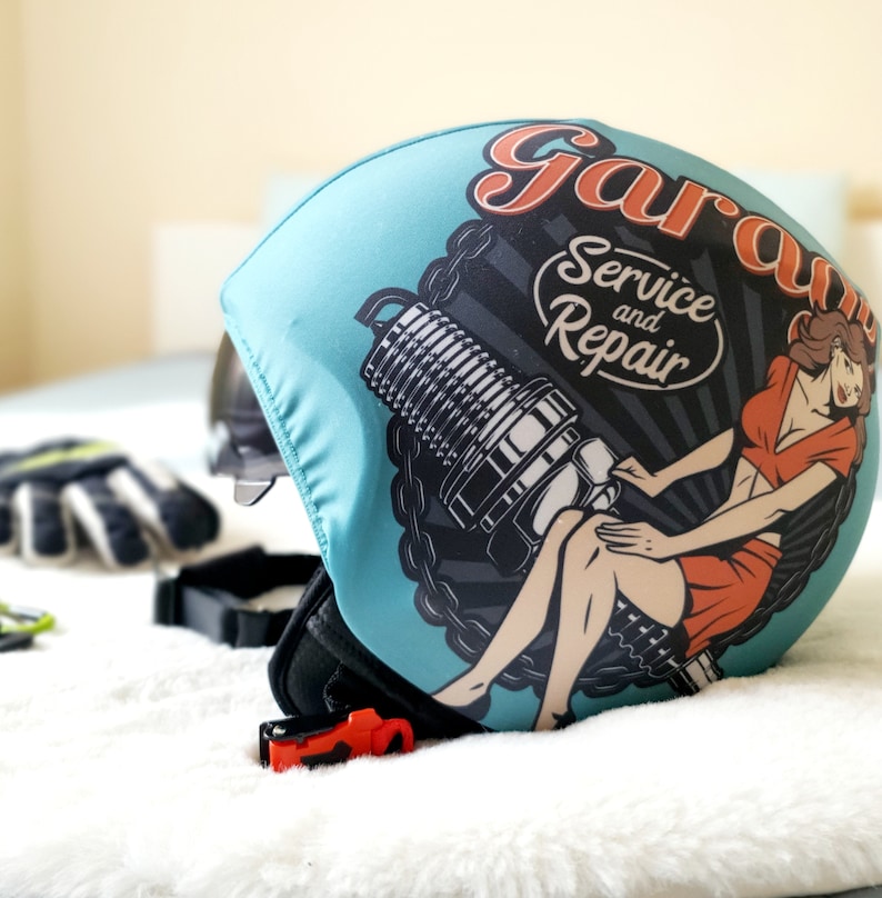 May include: A blue helmet with a graphic of a woman sitting on a spark plug with the text "Garage Service and Repair".