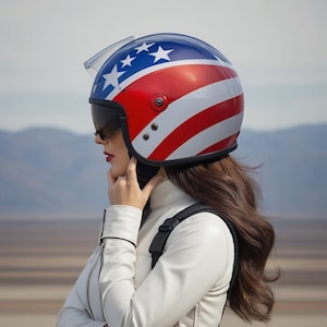 Pode incluir: Um capacete de motocicleta com um design patriótico da bandeira americana. O capacete tem uma parte superior azul com estrelas brancas, listras vermelhas e brancas e uma viseira transparente. Usado com uma jaqueta branca.