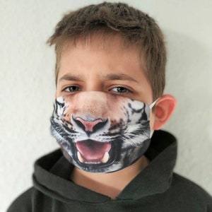 May include: A young person wearing a black hoodie with a white tiger face mask. The mask has a realistic design with a wide open mouth and sharp teeth.