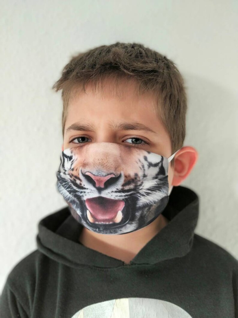 May include: A young person wearing a black hoodie with a white tiger face mask. The mask has a realistic design with a wide open mouth and sharp teeth.