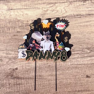 May include: A colorful cake topper featuring characters from "The Bad Guys" movie. The design includes a cityscape silhouette, diamonds, dollar signs, and the word "Danny 8". The topper is on two black sticks.