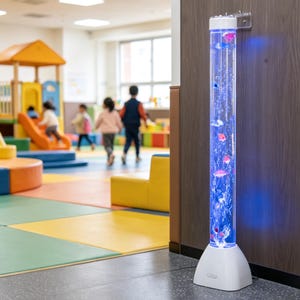 May include: A tall, white and clear bubble tube lamp with colorful, floating fish and bubbles. The lamp is illuminated with blue light and is mounted on a wall in a brightly colored playroom. Children are playing in the background.