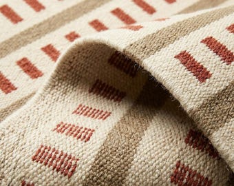 Puede incluir: Un tejido con un patrón repetitivo de rayas horizontales en color beige y crema, acentuado por filas de pequeños guiones rectangulares de color terracota. La tela tiene una textura visible de grano grueso con una esquina doblada.