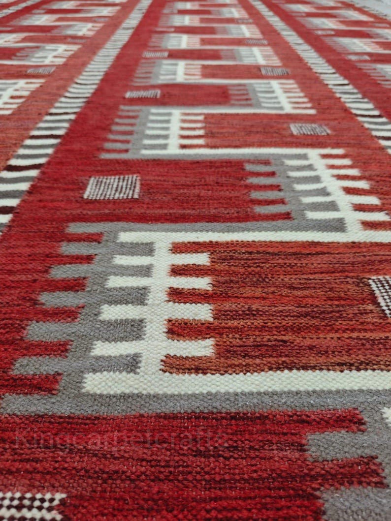 May include: A red, white, and gray geometric patterned rug. The rug features a repeating design of rectangles and lines in varying shades of red, white, and gray. The rug's texture appears to be woven.