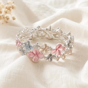 Peut inclure: Un bracelet en métal argenté orné d'un motif floral répétitif. Les fleurs sont finies avec de l'émail dans des tons de rose tendre, bleu clair et beige. De petits cristaux transparents sont sertis entre les pétales pour un éclat subtil.
