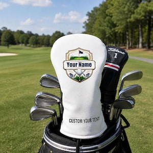 Könnte beinhalten: Eine weiße Golfschlägerhaube mit einem zentralen Emblem, das einen Golfball, Schläger und eine Flagge zeigt. Das Emblem enthält den Text "YOUR NAME" und der untere Teil der Haube zeigt den schwarzen Aufdruck "CUSTOM YOUR TEXT".