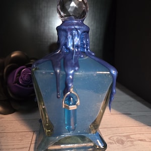 May include: A blue glass bottle with a faceted crystal stopper and a blue pendant. The bottle is decorated with dripping blue paint. The bottle is a unique decorative item.