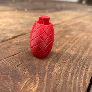 Könnte beinhalten: Ein roter Flaschenverschluss mit einem Rautenmuster. Der Verschluss hat eine zylindrische Form mit einem kleinen, rechteckigen Oberteil. Das Design ist in die Oberfläche geschnitzt. Der Verschluss besteht aus einem festen Material.