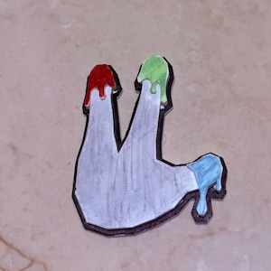 May include: A white, abstract-shaped object with a black outline, featuring red, green, and blue paint drips. The design has a textured appearance, suggesting a 3D-printed or crafted item. The overall aesthetic is modern and artistic.