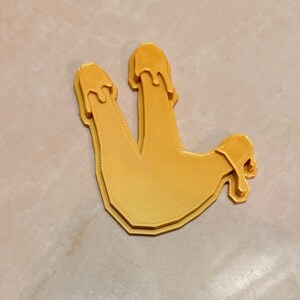 May include: A 3D-printed, yellow, stylized hand gesture with three fingers extended and dripping. The object has a textured surface and a layered design, suggesting a unique, artistic piece.