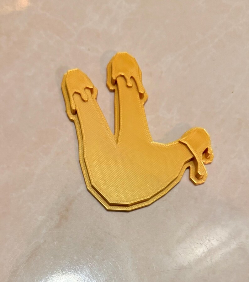May include: A 3D-printed, yellow, stylized hand gesture with three fingers extended and dripping. The object has a textured surface and a layered design, suggesting a unique, artistic piece.